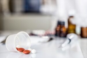 An incorrect dosage of pills spilling onto a table with syringes and other medications in the background