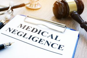 Medical negligence written on a blue clipboard next to a stethoscope and gavel hammer.